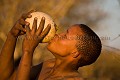 Jeune chasseur Bushman du désert du Kalahari au Botswana, en train de boire l'eau contenu dans un oeuf d'autruche. L'eau contenue dans l'oeuf qui est enterré dans un endroit stratégique, est incroyablement fraiche. Pour éviter que l'eau ne tourne et pourrisse dans l'oeuf (car elle peut rester stockée assez longtemps sous terre), l'orifice est obturé avec des feuilles d'un arbuste spécial au pouvoir antiseptique... Afrique 
 Africa 
 désert 
 desert 
 Botswana 
 gens 
 people 
 native 
 bushman 
 bushmen 
 Kalahari 
 traditionnal 
 tradition 
 diamont 
 diamants 
 brousse 
 bush 
 ADN 
 origine ,
eau,
water, 
drinking,
boire,
oeuf,
egg,
Autruche,
Ostrich,
chasseur,
homme,
San,
jeune,
 